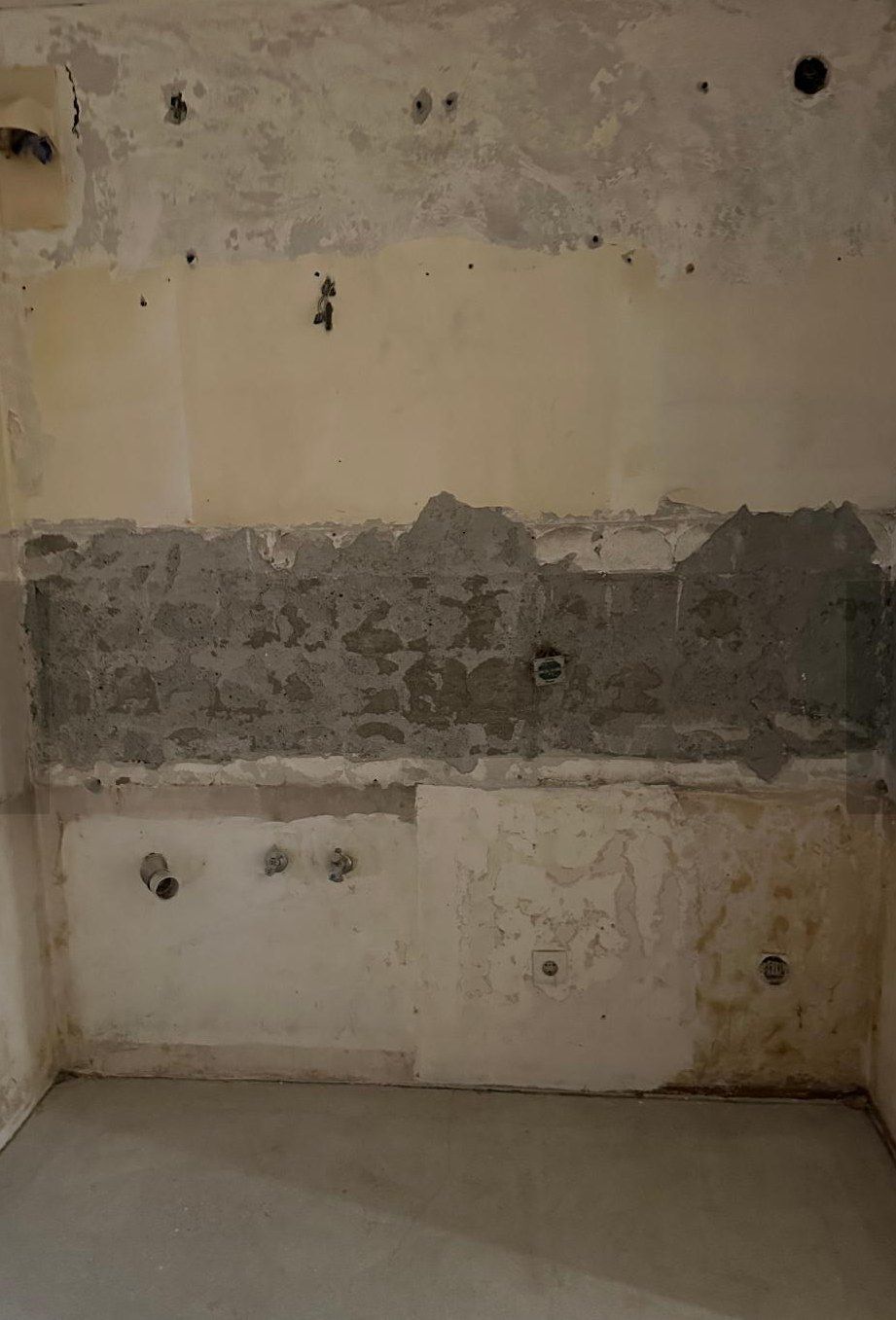 Badwand im entkernten Zustand: Fliesen und Putz abgeschlagen, Mauerwerk offen, Rohrstutzen und Anschlussdosen ragen aus der Wand.