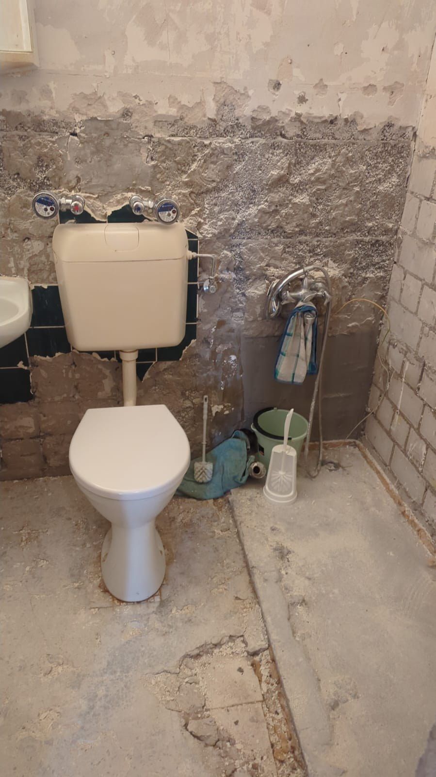 Altes WC vor dem Rückbau: Keramik mit Aufputzspülkasten vor einer teilweise abgeschlagenen Fliesenwand, freiliegendes Mauerwerk, aufgebrochener Boden.