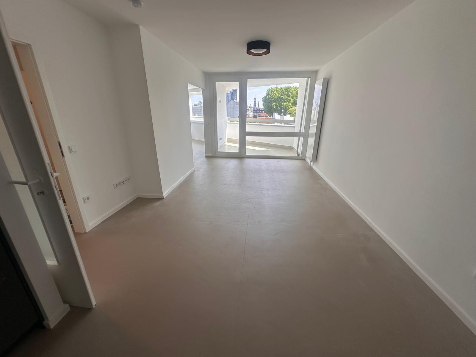 Fertiger Wohnraum nach der Kernsanierung: durchgehender heller Bodenbelag, weiße Wände, bodentiefe Balkontür zum Loggienausschnitt, Blick über die Dächer bis zum Turm der Michaeliskirche.