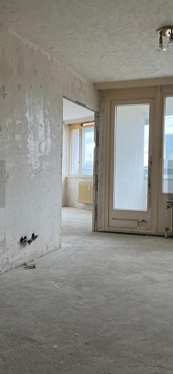 Wohnraum vor der Sanierung: Wände bis auf den alten Putz abgetragen, offener Estrich, alte Balkontür und Gussheizkörper, Durchgang ohne Zarge.