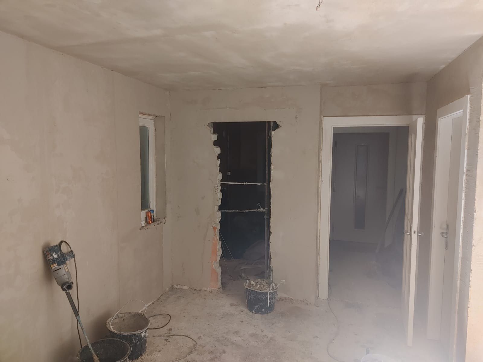 Aufgestemmter Wanddurchbruch im Rohbau: offene Öffnung mit sichtbaren Ziegeln und Trägerprofilen, verputzte Wände, Eimer und Bohrhammer am Boden.